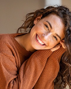 Woman in brown sweater smiling at home