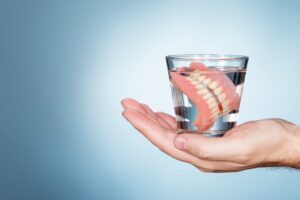 Hand holding a glass of water with a full set of dentures